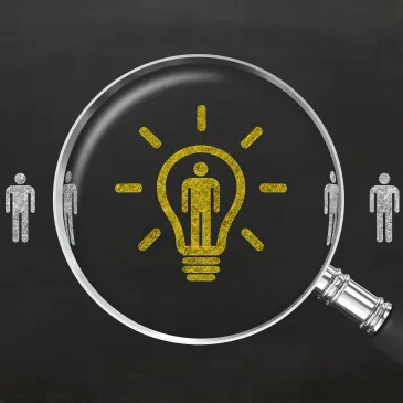 Magnifying glass highlighting a lightbulb with a person inside on a chalkboard.