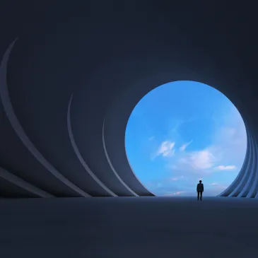 Person standing inside a large circular tunnel opening to a blue sky.